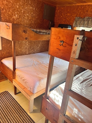 Un lit superposé avec une tête de lit et des tiroirs en bois, un mur en bois, une petite étagère et une fenêtre avec un rideau à rayures.