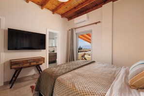 A bedroom with a bed, a TV mounted on the wall, a wooden dresser, and a window with a view. - Charming sea view private villa in Kato Korakiana, Corfu, 
quiet green area . (Kato Korakiana)