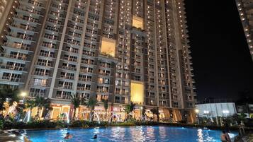 A high-rise hotel with a swimming pool, multiple balconies, and illuminated windows.