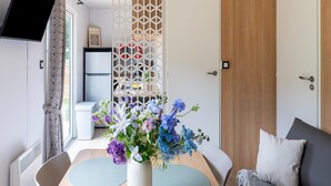 A modern room with a flat-screen TV, a white door, a wooden wardrobe, and a table with a vase of flowers. - Comfortable Caravan in a Green Setting (Kaprijke)