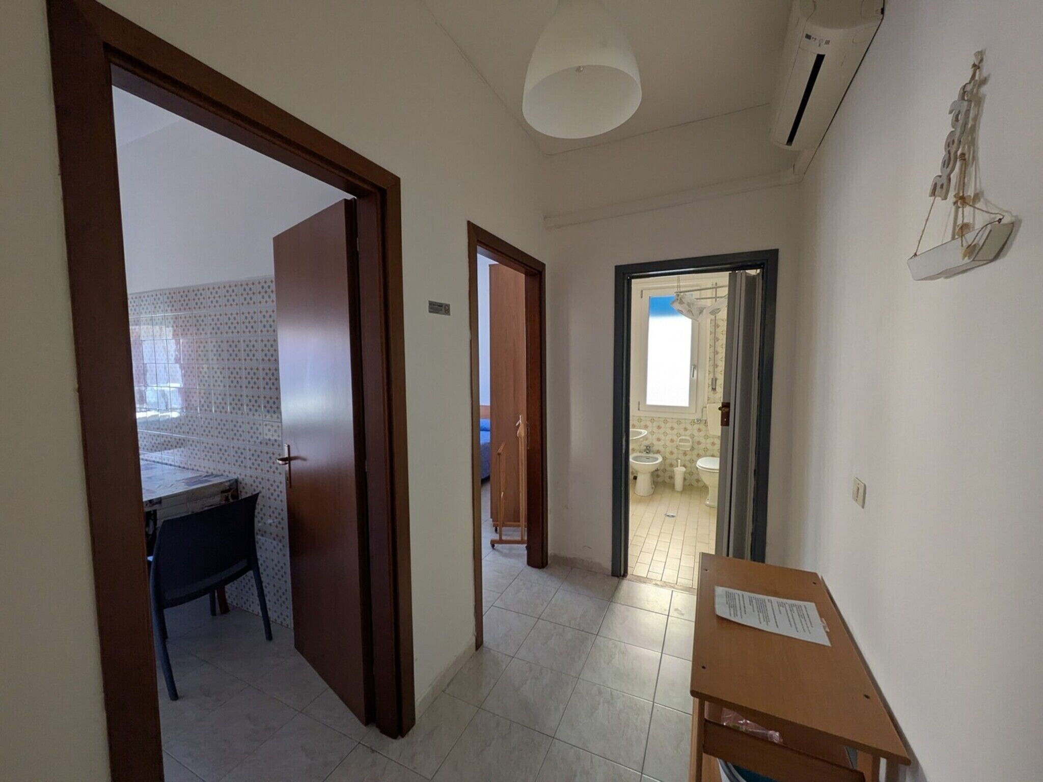A hallway with a wooden door, a small table with a paper, and a bathroom visible through an open door.
