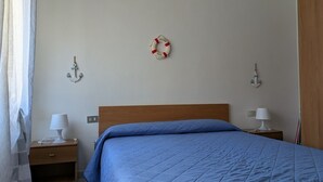 Une chambre à coucher avec un lit en bois, deux tables de chevet avec des lampes, une décoration murale représentant un dispositif de sauvetage et une décoration en forme d’ancre.