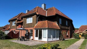 A two-story house with a covered patio, a brick exterior, and a gravel driveway. - Ferienwohnung in Petersdorf auf Fehmarn (Petersdorf)