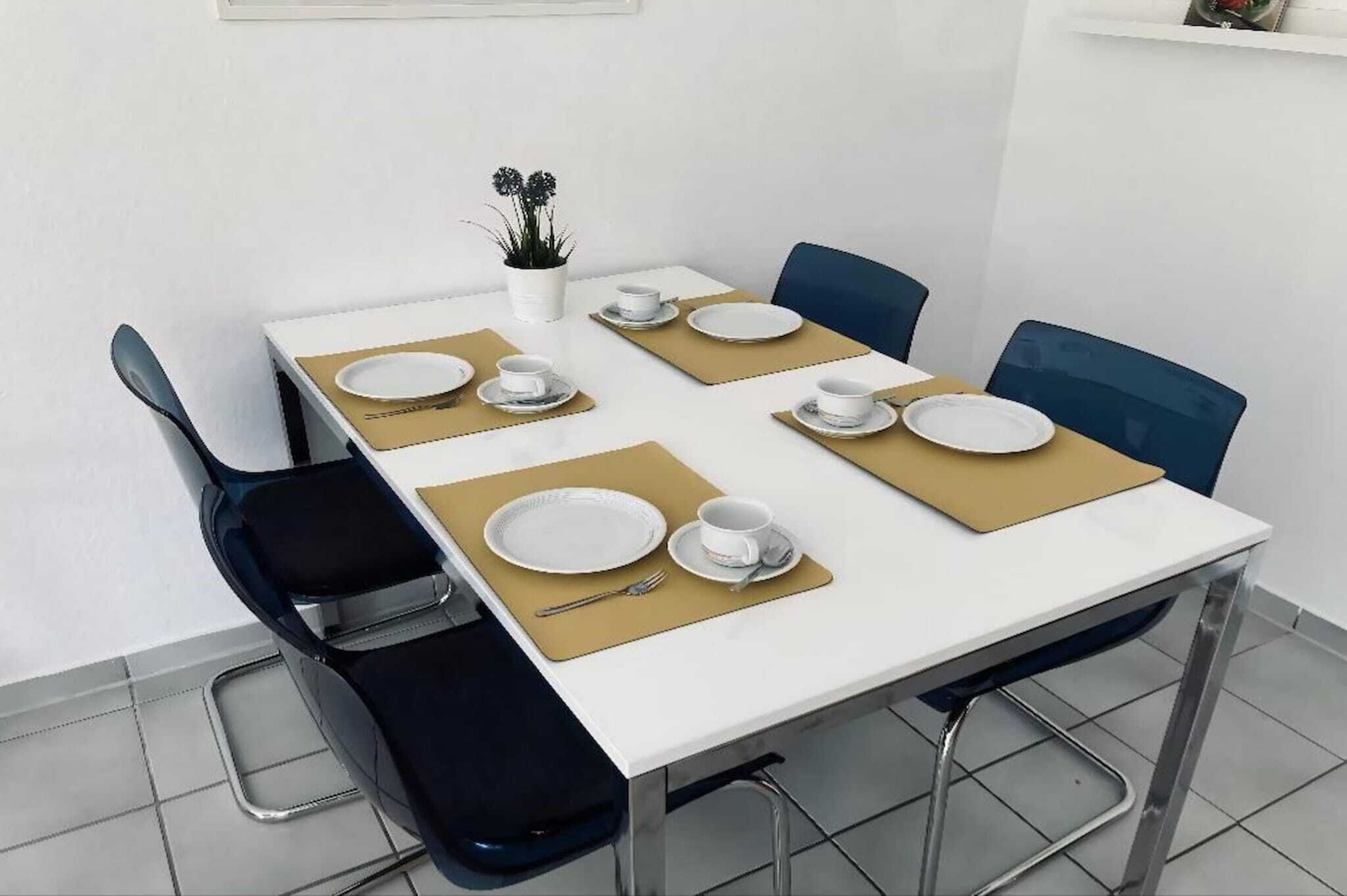 Una mesa de comedor dispuesta con platos, tazas y cubiertos, rodeada de sillas.
