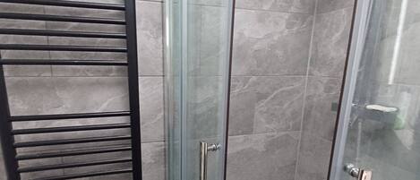 A glass-enclosed shower with a metal rack, a showerhead, and a tiled floor.