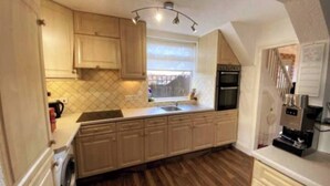 A kitchen with wooden cabinets, a washing machine, a coffee machine, and a window. - Room-furnished Spacious Double Room Near (Coventry)