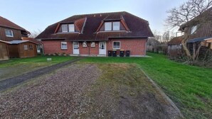 A two-story house with a sloped roof, a front porch, and a gravel driveway. - Ferienwohnung in Petersdorf auf Fehmarn (Petersdorf)