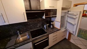 A modern kitchen with a stove, sink, and microwave. - Ferienwohnung in Petersdorf auf Fehmarn (Petersdorf)