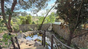 Un puente de madera que conduce a un muro de piedra con una estatua de Buda, rodeado de follaje y un pequeño estanque.