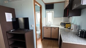 Cocina compacta equipada con microondas, tostadora y lavamanos. Hay un televisor en un estante y una puerta que da al baño.