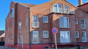 Un immeuble en briques à plusieurs étages, doté de balcons, d’un panneau indiquant qu’il est interdit de se garer et d’un lampadaire.
