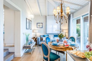 A dining area with a wooden table set for a meal, a chandelier, and a view through a glass door. - Villa in Sardinia Near Porto Ottiolu Beach (Budoni)