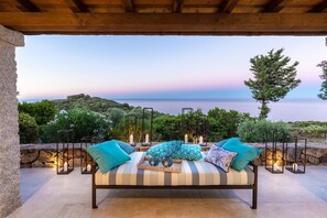 A bed with pillows and candles, a stone wall, and a view of the sea. - Villa in Sardinia Near Porto Ottiolu Beach (Budoni)