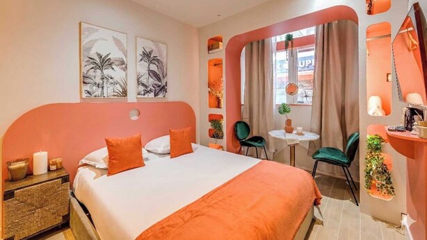 Une chambre d’hôtel avec un lit, une petite table, des chaises, un miroir et des œuvres d’art accrochées aux murs.