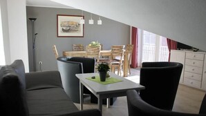 A modern living room with a dining area, a sofa, a table with a plant, and a painting on the wall. - Ferienwohnung in Orth auf Fehmarn (Orth)