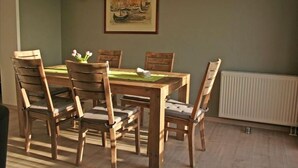 A dining area with a wooden table and chairs, a framed painting on the wall, and a radiator below. - Ferienwohnung in Orth auf Fehmarn (Orth)
