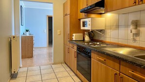 A kitchen with wooden cabinets, a microwave, a toaster, and a stove. - Ferienwohnung in Orth auf Fehmarn (Orth)