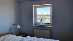 A bedroom with a window, a radiator, a lamp, and a bed. - Ferienwohnung in Orth auf Fehmarn (Orth)