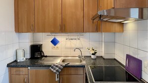 Keittiössä on puukehikoiset kaapit, ruostumattomasta teräksestä valmistettu liesituuletin, pesuallas, kahvinkeitin ja pieni ruukkukasvi.