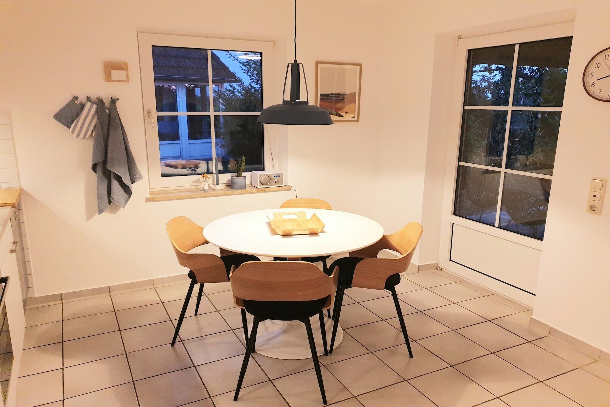 Ein Essbereich mit einem runden Tisch, vier Stühlen, einer Hängelampe, einem Fenster mit Aussicht und einer Wanduhr.