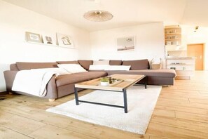 A modern living room with a sectional sofa, a coffee table, and a kitchen area in the background. - Ferienwohnung in Lemkenhafen auf Fehmarn (Lemkenhafen)