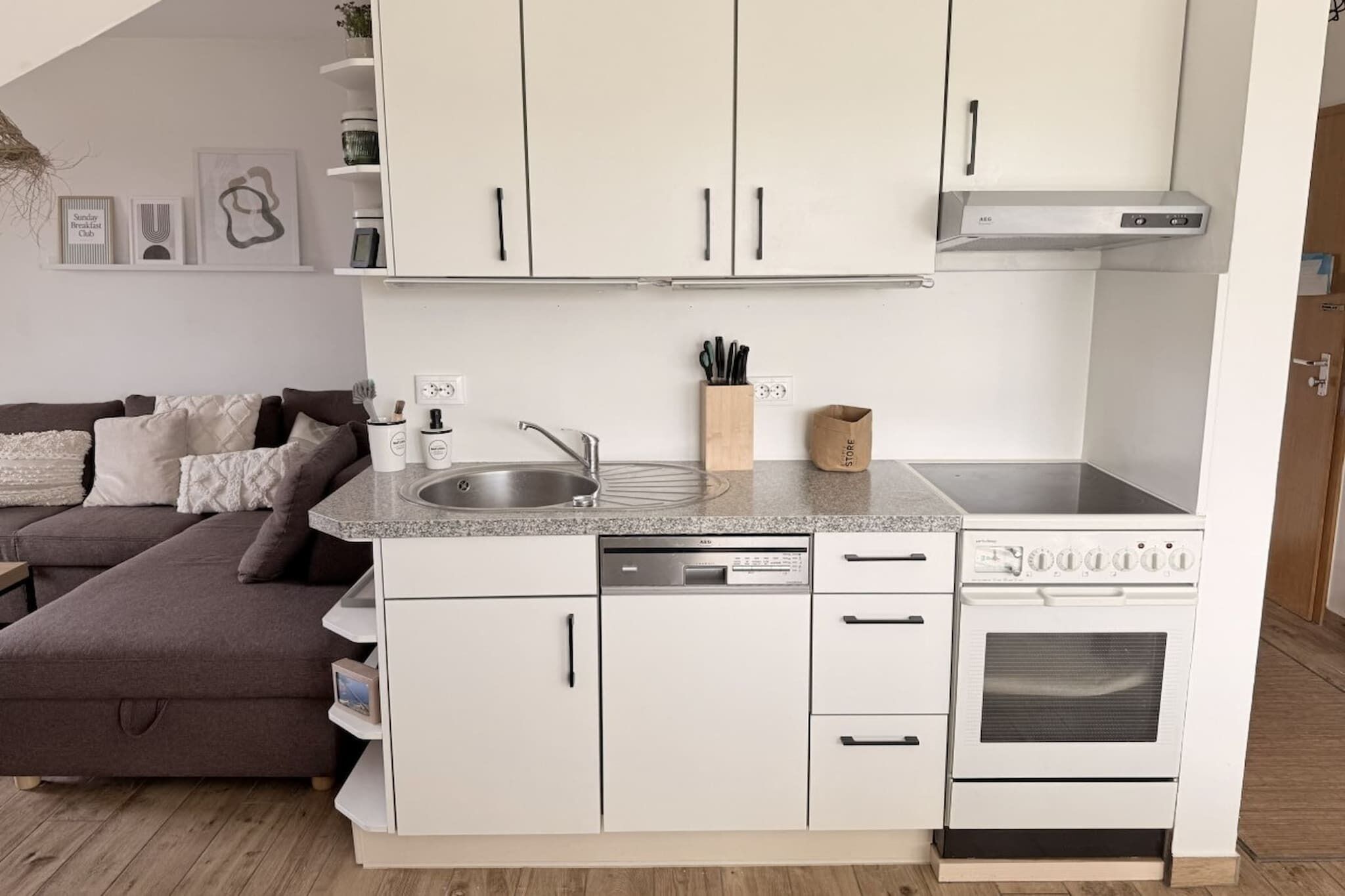 Cocina compacta con armarios blancos, lavavajillas integrado, estufa y encimera con lavabo.