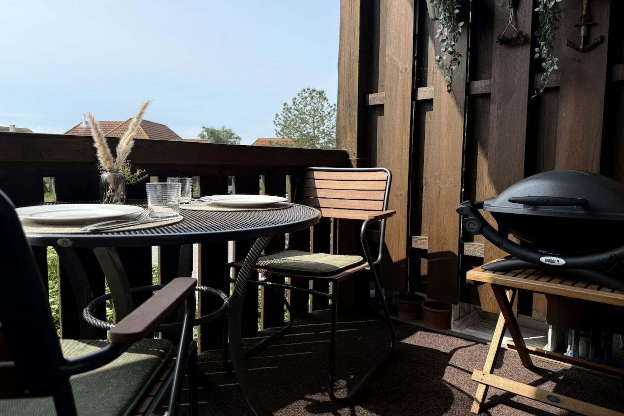 An outdoor patio with a round table, chairs, a grill, and a wooden pergola.