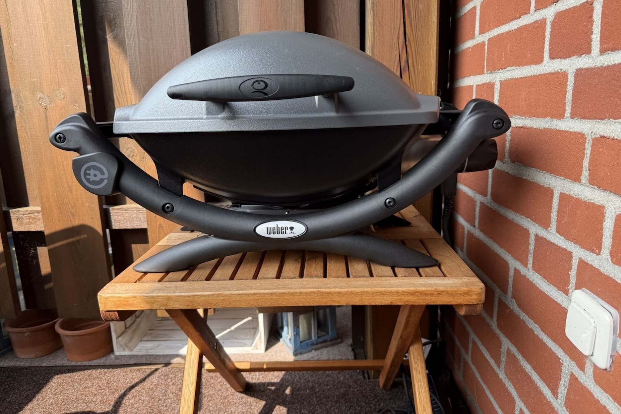 Ein Weber-Grill auf einem Holztisch vor einer Backsteinmauer.