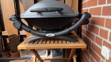 Ein Weber-Grill auf einem Holztisch vor einer Backsteinmauer.
