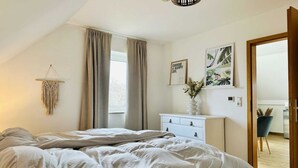 Un dormitorio con cama, cómoda, tapiz de macramé y puerta que da a otra habitación.