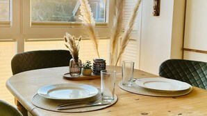 Una mesa de comedor dispuesta con platos, cubiertos y vasos, con decoraciones de hierba de pampa y una pequeña planta sobre una bandeja.
