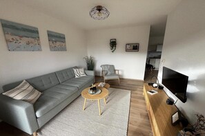 Un salon avec un canapé gris, une petite table basse ronde, un téléviseur et une bibliothèque.