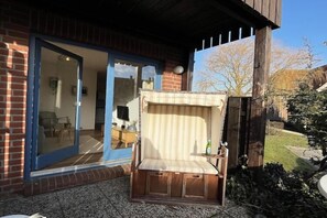 A wooden bench with a cushion outside a house with a glass door. - Ferienwohnung in Lemkenhafen auf Fehmarn (Lemkenhafen)