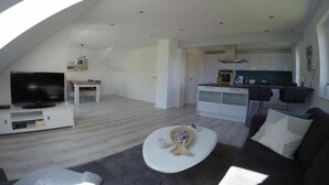 Ein großzügiger Wohnbereich mit Flachbildfernseher, weißem Couchtisch und dunklem Sofa.