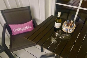A table with a bottle of wine, two wine glasses, and a basket of wine corks. - Ferienhaus in Westermarkelsdorf auf Fehmarn (Westermarkelsdorf)