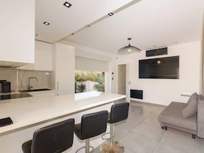 Een moderne keuken met een centraal eiland, barkrukken, een bank en een aan de muur bevestigde televisie.