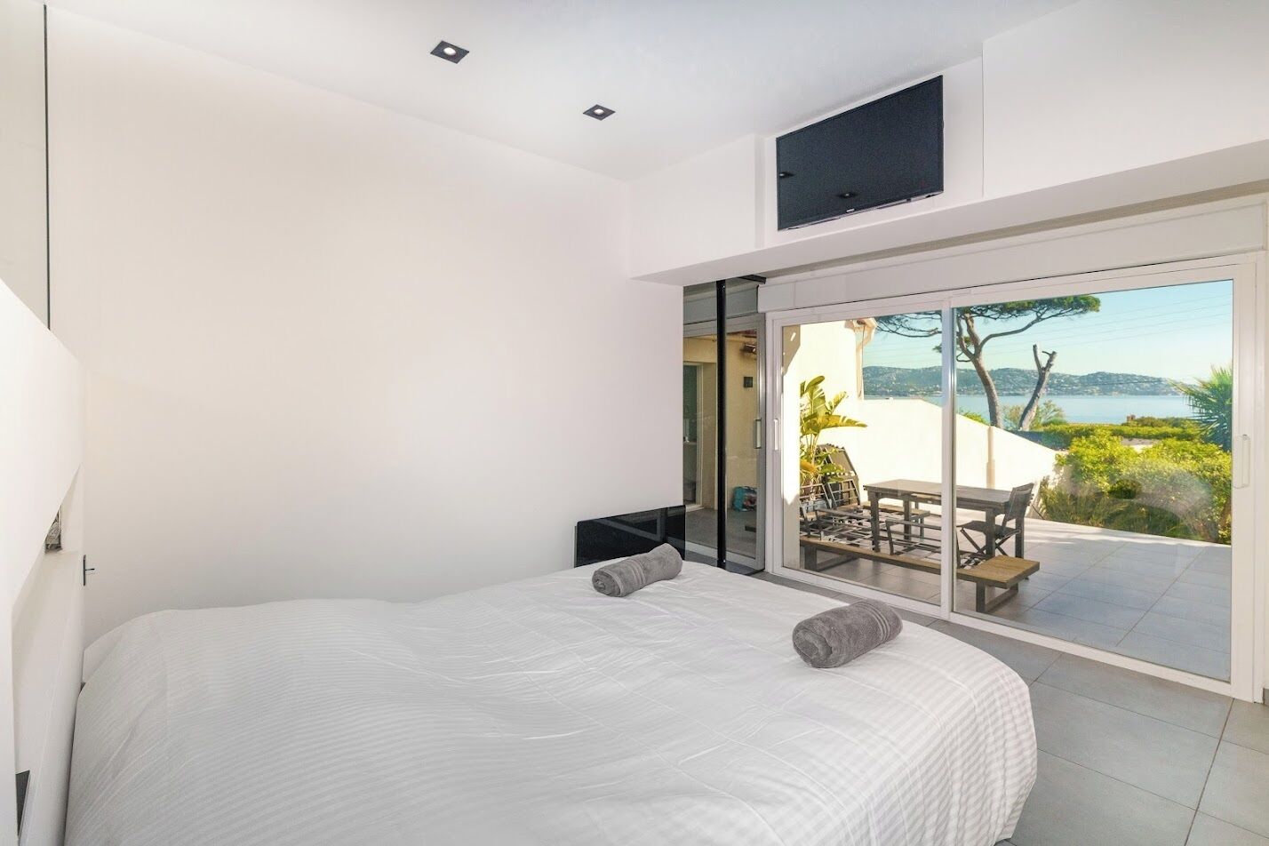 Een slaapkamer met een groot bed, een televisie en een schuifpui die uitkomt op een buitenpatio met een tafel en stoelen.
