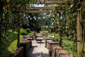 Ein Gartenweg mit Ziegelmauern, einer Feuerstelle und hängenden Laternen.