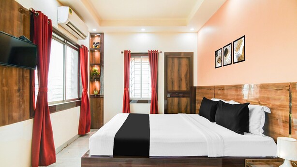 A hotel room with a wooden bed, red curtains, a television, a wall-mounted air conditioner, and framed artwork. - Super Deluxe Room More Bimla Regency (Barakpur)