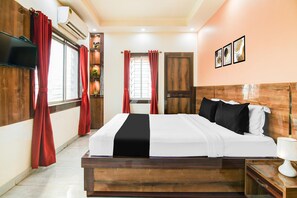 A hotel room with a wooden bed, red curtains, a television, a wall-mounted air conditioner, and framed artwork.