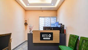 A hotel reception desk with a sign reading 'HOTELO Company Serviced,' a window with blinds, and green chairs. - Super Deluxe Room More Bimla Regency (Barakpur)