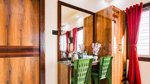 A room with a wooden wardrobe, a dining table with chairs, and red curtains. - Super Deluxe Room More Bimla Regency (Barakpur)
