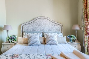 A neatly made bed with a floral bedspread, two nightstands with lamps, and a decorative headboard. - Apartment in Lucca Near Guinigi Tower (Lucca)