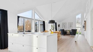 A modern kitchen with a large island, a dining area with a table and chairs, and a staircase leading to an upper level. - 4 Star Holiday Home in Rude (Bisserup)