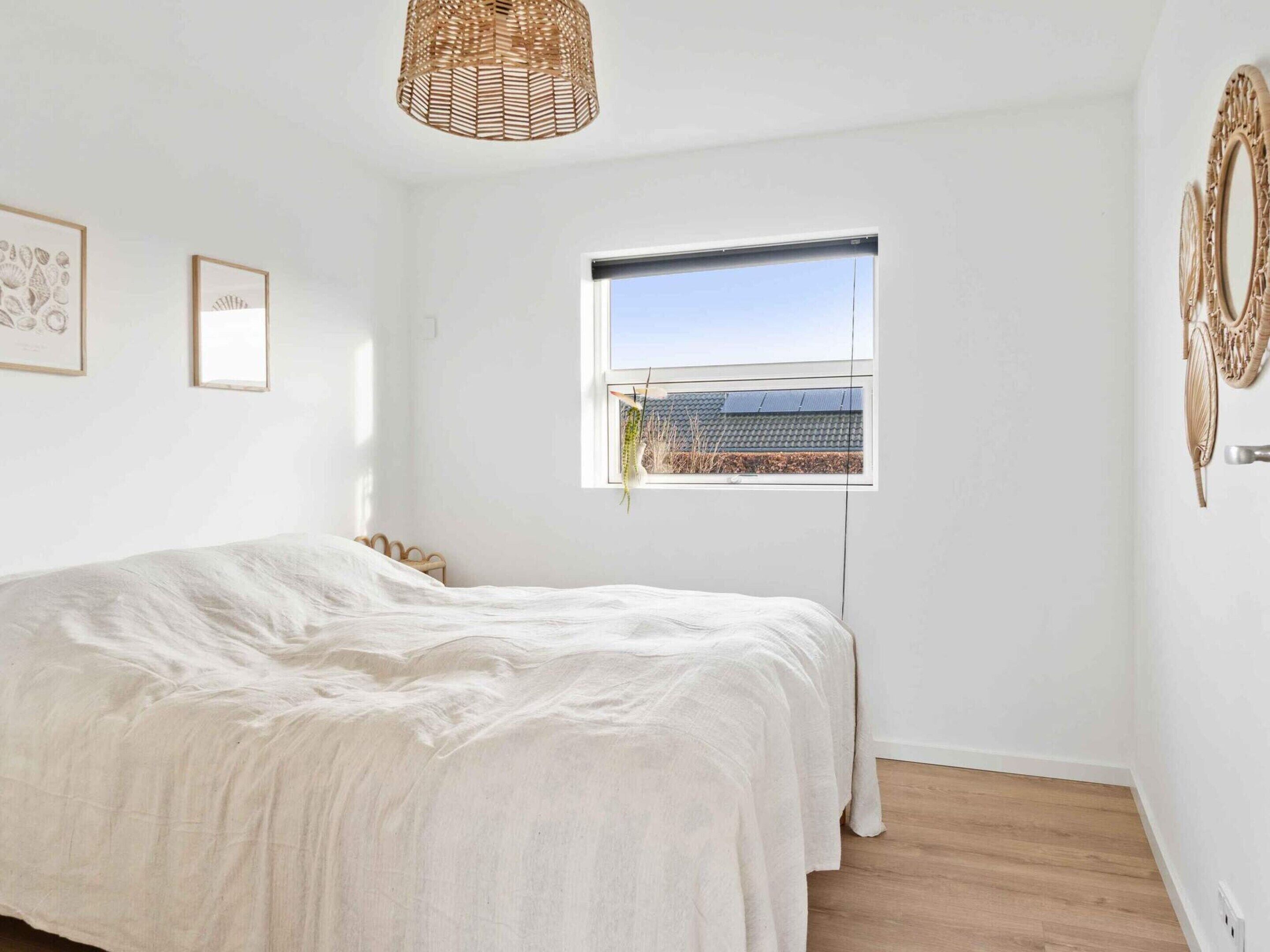 A bedroom with a bed, a window, a woven light fixture, and wall-mounted decor.