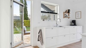 A modern kitchen with a large window, white cabinetry, and a coffee machine. - 4 Star Holiday Home in Rude (Bisserup)