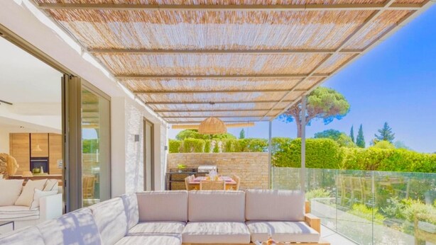 Un espace de vie extérieur moderne comprenant un grand canapé, une table à manger et un barbecue.