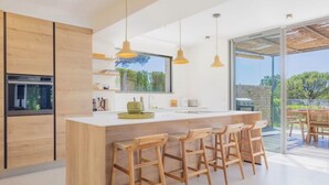 Une cuisine moderne dotée d’un grand îlot central, de tabourets de bar en bois, de luminaires suspendus et offrant une vue sur l’extérieur.