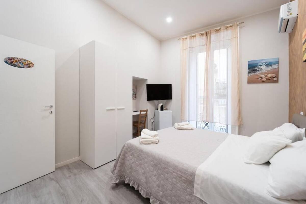 Quarto com cama, escrivaninha, televisão e janela com cortinas.
