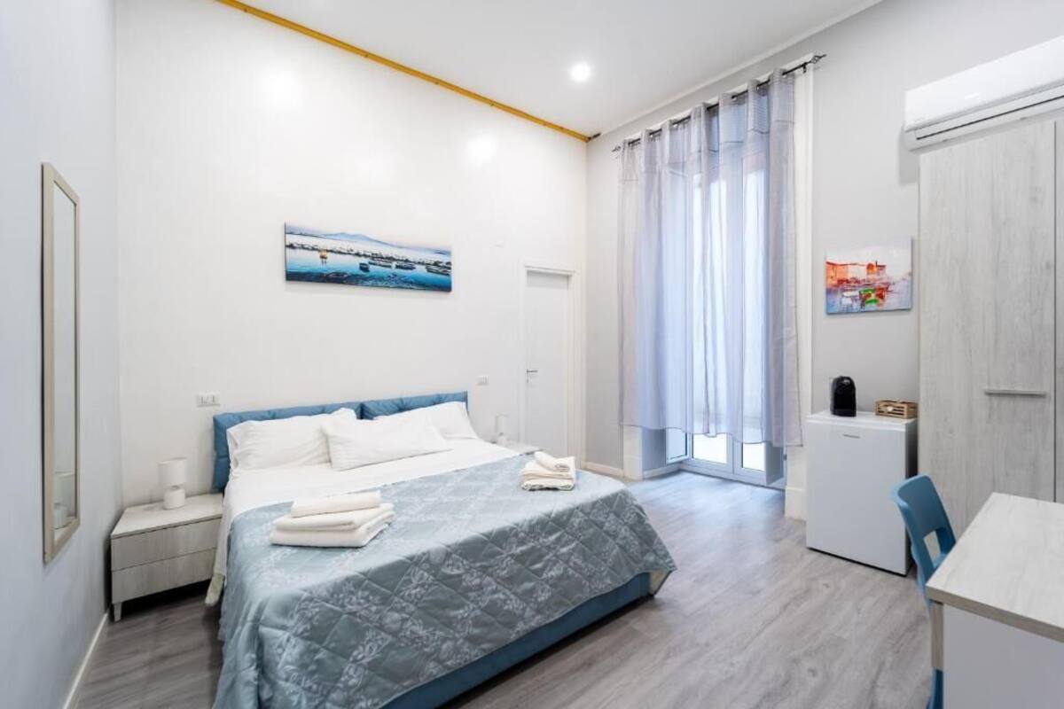 Quarto com cama, mesa de cabeceira e pequena escrivaninha com cadeira.